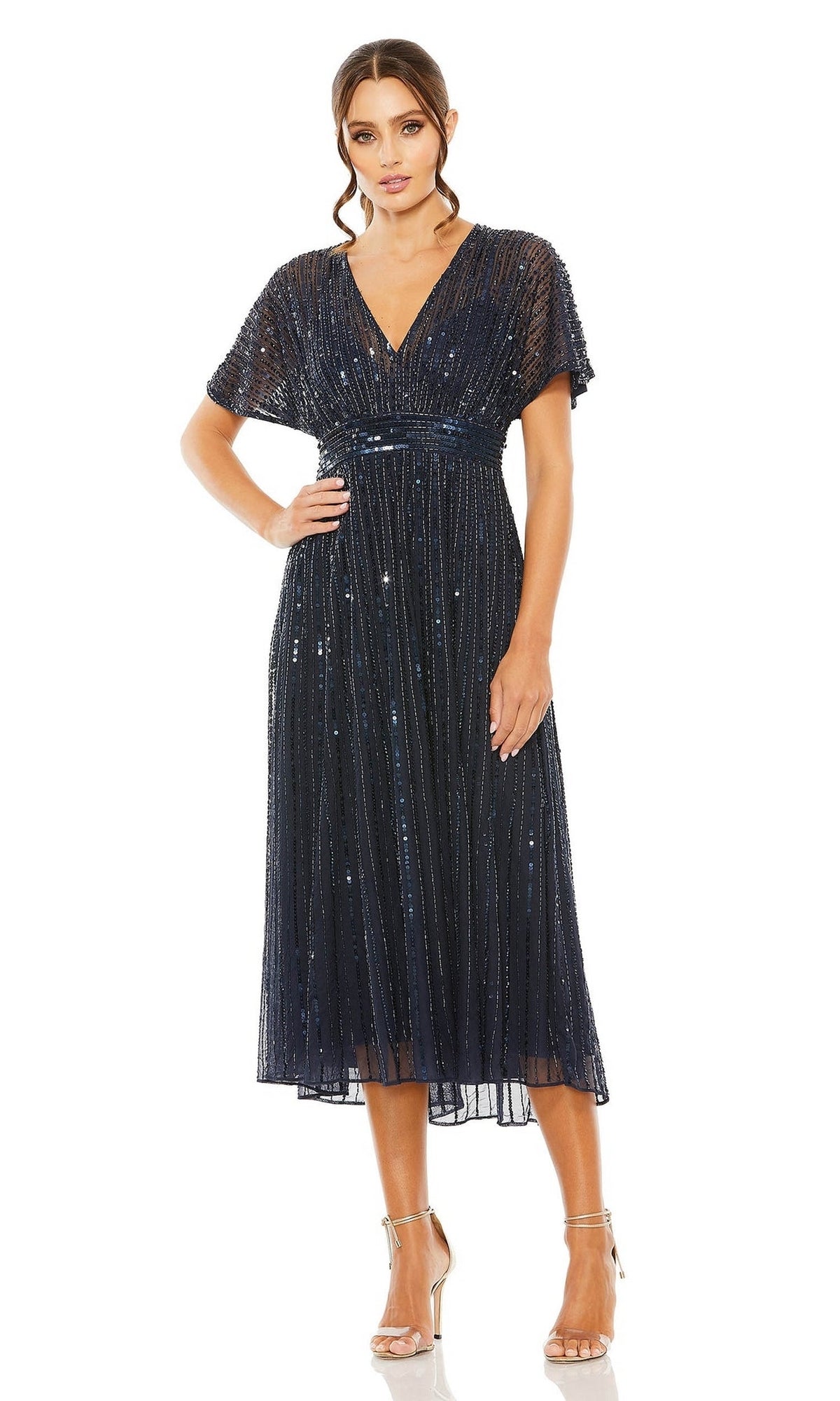 Woman in the Mac Duggal 14007 Short Sequin Wedding-Guest Dress—dark blue, knee-length, short-sleeved with V-neck and vertical detail—paired with silver heels against a white background; an ideal semi-formal party look.